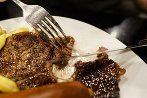 Mann Essen gegrillt Fleisch Anteil von Platte. Hand halten Messer und Gabel Schneiden gegrillt Rindfleisch Steak foto