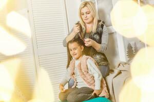 glücklich liebend Familie. Mutter ist Kämmen ihr Tochter Haar Sitzung durch das Fenster im das Kinder- Zimmer foto