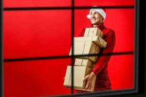 Porträt von einer gut aussehend Neu Jahr Mann im rot Santa claus Weihnachten Hut Fenster Weihnachten foto