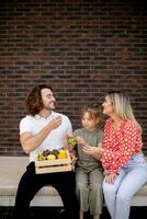 Familie mit ein Mutter, Vater und Tochter Sitzung draußen auf das Schritte von ein Vorderseite Veranda von ein Backstein Haus foto