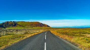 Panorama- Über ein gepflastert Straße und isländisch bunt und wild Landschaft mit Fjorde und Meer beim Sommer- Zeit, Westen Island foto