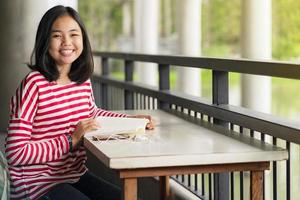 asiatisches studentenmädchen, das in der schule ein buch liest und lächelt foto