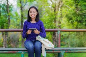 asiatisches studentenmädchen, das an einem sonnigen sommertag ein digitales tablet im park verwendet foto