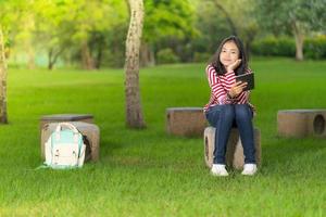 asiatisches studentenmädchen mit einem digitalen tablet im schulpark an einem sonnigen sommertag foto