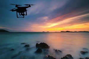 Silhouette der Drohne, die bei Sonnenuntergang über das Meer fliegt foto