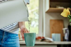 Frau Gießen Wasser von Kessel zum brauen Tee foto