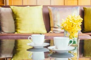 Vase Blume und weiße Kaffeetasse auf Tisch und Kissen auf Sofa