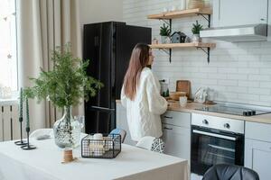 Frau in warmweißem Winterpullover, die zu Hause in der Küche steht foto