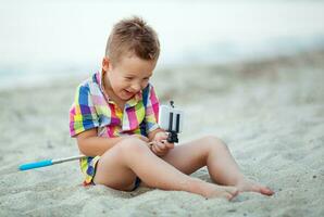 glücklich Junge mit Selfie Stock und Zelle beim das Strand foto