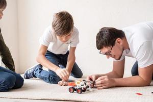 Vater und Jungen haben Spaß daran, Roboterautos zu Hause zu bauen, die auf dem Teppich sitzen sitting foto