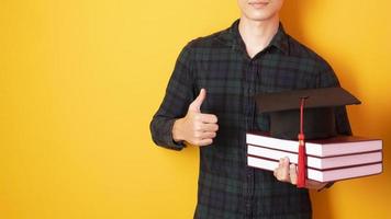 Universitätsmann ist glücklich mit Abschluss auf gelbem Hintergrund foto