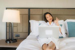 Porträt schöne junge asiatische Frauen mit Laptop oder Computer mit Smartphone auf dem Bett foto