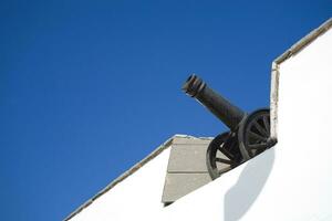 alt Antiquität schwarz Kanone auf ein Weiß Mauer mit ein Blau Himmel Hintergrund foto
