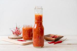 Chili oder Chilisauce in Flasche und Glas auf Holzhintergrund on foto