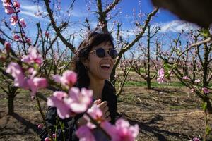Frau lächelt unter das ziemlich Rosa Blumen von das Pfirsich Baum. foto
