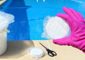 ein Weiß groß Chlor Tablette im das Hand von ein lila schützend Handschuh von ein Schwimmbad Desinfektion Bedienung Arbeiter. das Anfang von das Schwimmen Jahreszeit im das heiß Sommer- auf Urlaub. foto