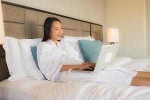 Porträt schöne junge asiatische Frauen mit Laptop oder Computer mit Smartphone auf dem Bett foto