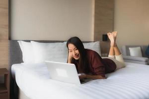 Portrait schöne junge asiatische Frauen mit Computer und Handy auf dem Bett foto