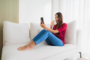 Portrait schöne junge asiatische Frauen mit Handy oder Smartphone auf dem Sofa foto