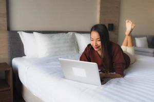 Portrait schöne junge asiatische Frauen mit Computer und Handy auf dem Bett foto