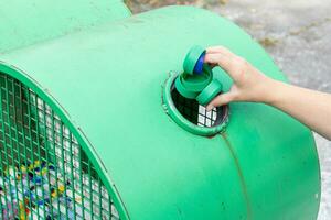 Hand werfen Plastik Kappen in ein städtisch Recycling Behälter. Umgebung und global freundlich Konzept foto