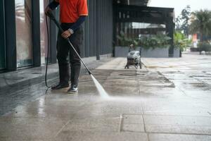 Reinigung Mitarbeiter Schläuche ein tragbar Auto zum Waschen das Beton Fußboden mit hoher Druck Wasser Jets. foto