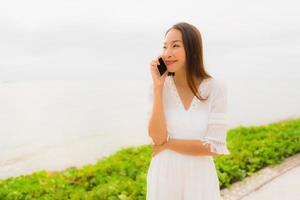 Porträt schöne asiatische Frau Hut mit Lächeln glücklich für das Telefonieren am Strand foto