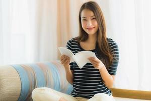 Porträt der schönen jungen Asiatin, die ein Buch auf dem Sofa im Wohnzimmer liest foto