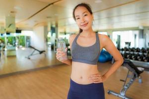 Porträt schöne junge asiatische Frau mit Flaschenwasser im Fitnessstudio foto