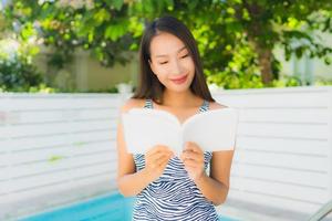 Porträt schöne junge asiatische Frau glückliches Lächeln mit Lesebuch rund ums Schwimmbad foto