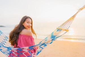 Porträt schöne junge asiatische Frau sitzt auf der Hängematte mit einem Lächeln glücklich in der Nähe von Strand Meer und Ozean foto