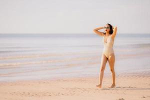 Porträt junge schöne asiatische Frau zu Fuß Lächeln glücklich am Strand Meer Ozean mit Sonnenbrille foto