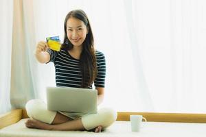 Porträt schöne junge asiatische Frau mit Computer-Notebook oder Laptop mit Kreditkarte zum Einkaufen foto