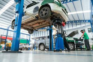 Auto Mechaniker Arbeiten im Auto Reparatur Bahnhof gepflastert mit Epoxid Fußboden und elektrisch Aufzug zum ein Auto Das kommt zu Veränderung das Motor Öl im das Hintergrund von Auto Reparatur Center mit Epoxid Etagen. foto