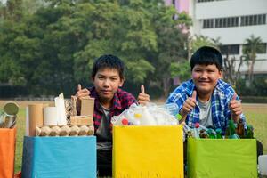 asiatisch Junge im Plaid Hemd Sitzung auf Spielplatz von Schule mit verschiedene Kisten von getrennt Garbabes oder Müll innen, Konzept zum Öko freunde und global Erwärmen Kampagne, Sanft und selektiv Fokus. foto