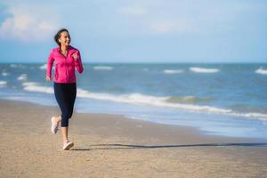 Porträt schöne junge asiatische Frau, die auf dem tropischen Naturstrand Meer Ozean läuft und trainiert foto