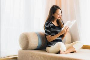 Porträt der schönen jungen Asiatin, die ein Buch auf dem Sofa im Wohnzimmer liest foto