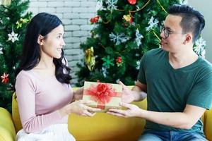 junges asiatisches paar gibt ein weihnachtsgeschenk. das konzept eines glücklichen lebens zu weihnachten foto