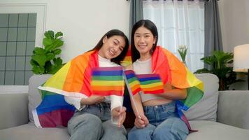 asiatisch jung schön ziemlich weiblich Lesben Sitzung Nieder und Sofa Flagge winken Regenbogen Gleichberechtigung Freiheit lgbtq Fröhlich stolz Stolz. foto