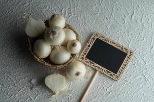 Zwiebeln in einer Holzschale mit kleinem schwarzen Brett auf strukturiertem Hintergrund. Inhaltsstoffe.