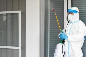 Arbeitnehmer von Dekontaminationsdiensten, die persönliche Schutzausrüstung oder PSA einschließlich Anzug, Gesichtsschutz und Maske tragen er verwendet Desinfektionsmittel, um das Wissenschaftlerlabor zu sprühen und zu reinigen foto