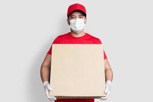 Liefermann-Mitarbeiter in roter Kappe leeres T-Shirt einheitliche Gesichtsmaske halten leeren Karton isoliert auf weißem Hintergrund
