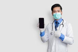 Arzt hält Telefon mit Daumen nach oben isoliert. pakistanischer mann arzt technologie medizin zu hause. Telefon klarer Bildschirm.