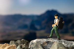 Miniaturreisender mit Rucksack, der auf den Felsen geht foto