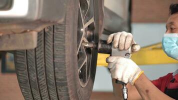 asiatisch Mann Auto Mechaniker ersetzen ein Auto Reifen im Garage Werkstatt. . Auto Service, Autopflege Center entfernt das Rad, Reparatur und Instandhaltung von das Auto im Service. foto