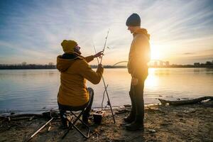 Vater und Sohn sind Angeln auf Winter Tag. Fluss Angeln. Teenager Junge ist Lernen zu Fisch. foto