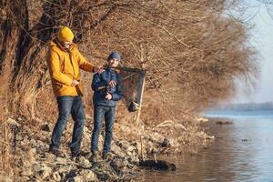 Vater und Sohn sind Angeln auf sonnig Winter Tag. Sie gefangen ein Fisch und sind halten es im ein Landung Netz. foto