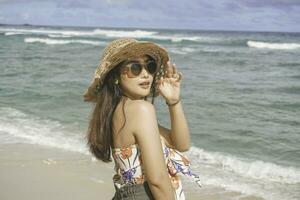 ein glücklich jung asiatisch Frau tragen Strand Hut ist posieren zu das Kamera beim das Strand im gunungkidul, Indonesien foto
