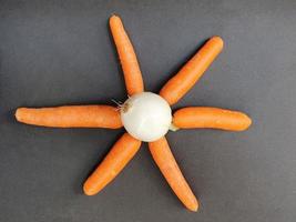 frische Karottengemüsestücke und eine weiße Zwiebel auf der schwarzen Oberfläche, frisches Gemüse natürlichen Ursprungs zur Zubereitung vegetarischer Speisen foto