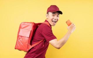 asiatischer Lieferbote, der eine rote Uniform trägt, die auf gelbem Hintergrund posiert foto
